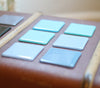 Powder blue opal fused art glass coaster 100x100mm size angled view on packing trunk